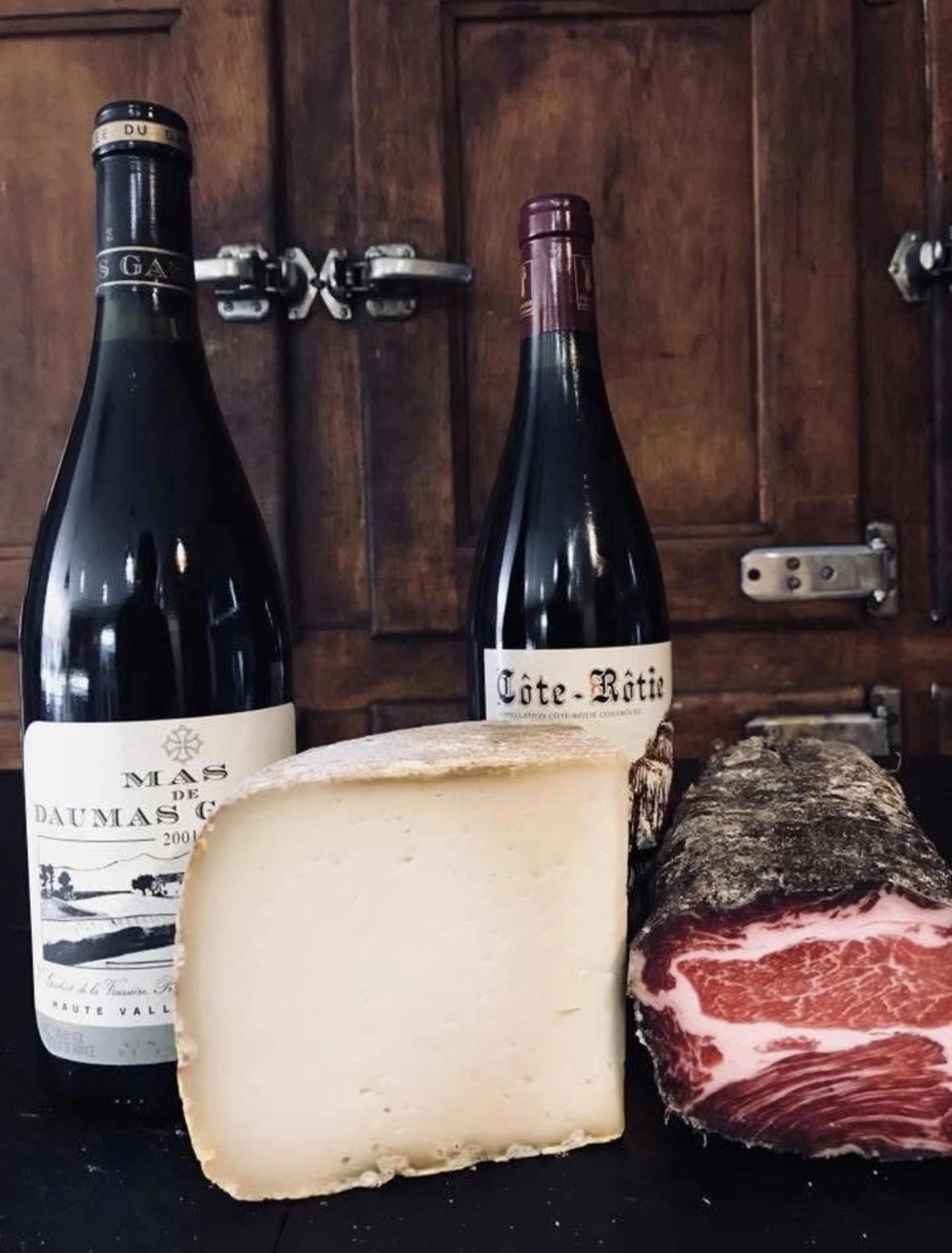 une image d'un fromage, d'une bouteille de vin et d'un saucisson côte à côte.